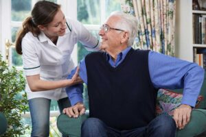 A caregiver assisting an elderly person with medication and daily health routines in a bright, homelike room.