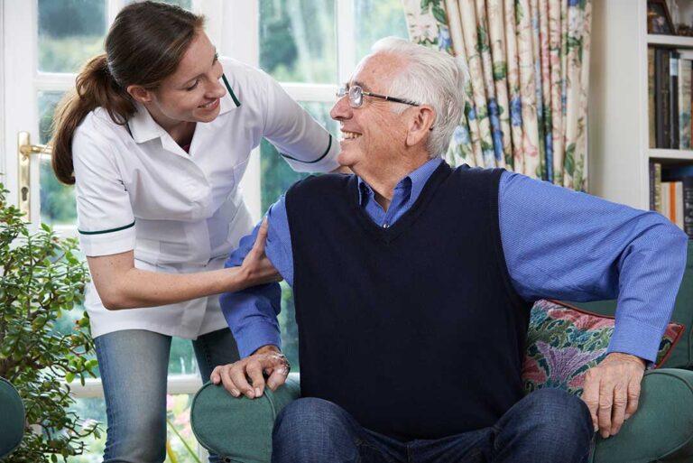 A caregiver assisting an elderly person with medication and daily health routines in a bright, homelike room.